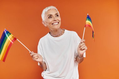 Büyüleyici olgun kadın gururu kucaklarken elinde şık bir elbiseyle gökkuşağı bayrakları tutuyor..