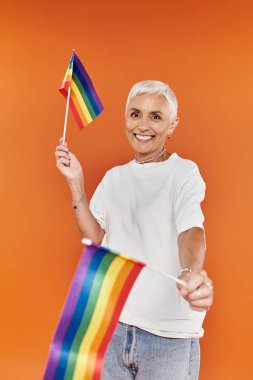 Olgun bir kadın sevinçle gökkuşağı bayrakları sallar, gurur ve mutluluğu somutlaştırır..