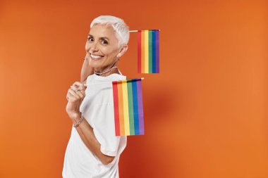 Kendinden emin bir kadın gururla desteğini gösterir, elinde gökkuşağı bayrakları.