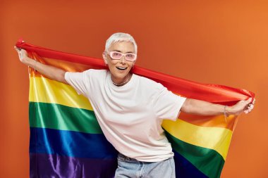 Neşeli bir kadın elinde bir gökkuşağı bayrağı, ışıl ışıl giyinmiş gururu ve kendine güveni olan.