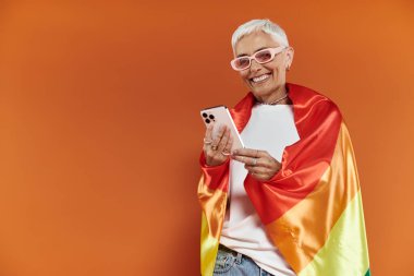 A mature woman radiates joy while wrapped in a rainbow flag. clipart