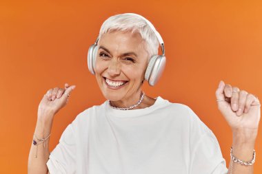 Kısa saçlı olgun bir kadın müzik dinlerken mutlu bir şekilde dans eder..