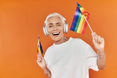 Havalı bir kadın elinde gökkuşağı bayraklarıyla mutlu bir şekilde dans eder..