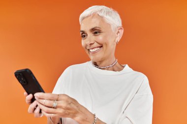 Kendine güvenen bir kadın, şık bir kıyafetle akıllı telefonunu kullanırken gülümser..