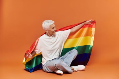 A mature woman embraces a rainbow flag with joy and confidence. clipart