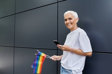 Neşeli kadın modern şehirlerde mesajlaşırken gurur bayrağı sallıyor.