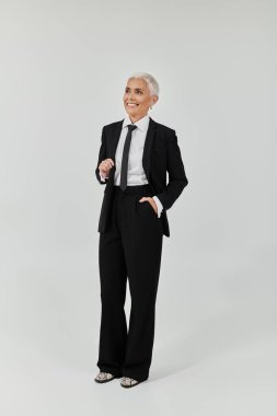 A mature woman with short hair showcases her chic outfit in a poised stance. clipart