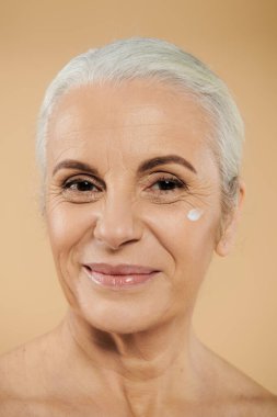 A mature woman applying cream on her face. clipart