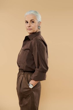 Kendine güvenen olgun bir kadın duruyor, tarzını ve duruşunu sergiliyor..