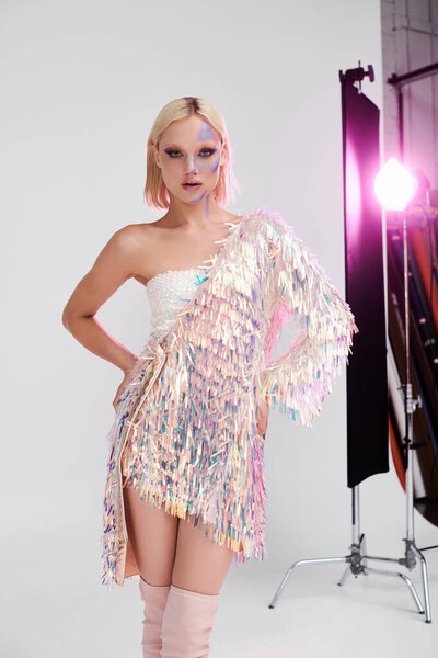Стильная молодая женщина уверенно позирует в блестящей одежде с голографическими деталями.