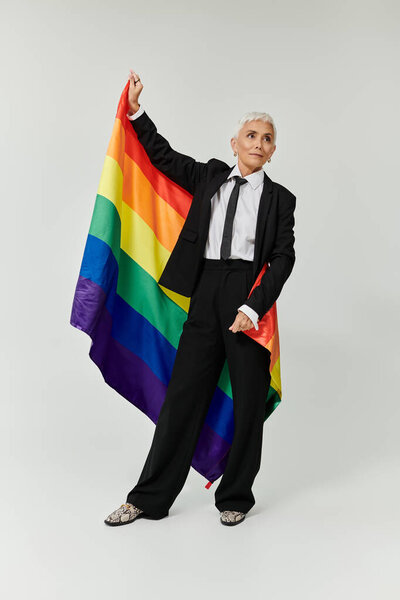 Confident woman with short hair proudly holding a rainbow flag.