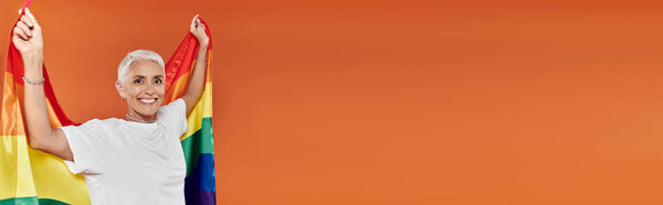 Mature woman joyfully waving a rainbow flag in a colorful expression of pride.