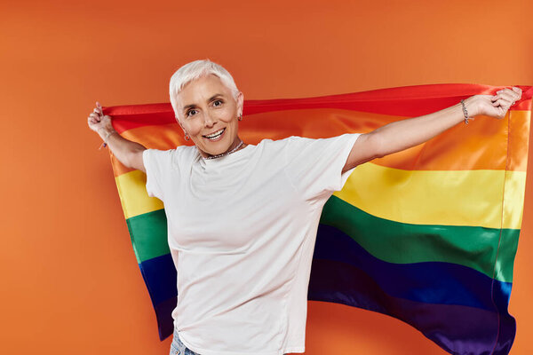 A confident woman proudly displays a rainbow flag in a lively atmosphere.