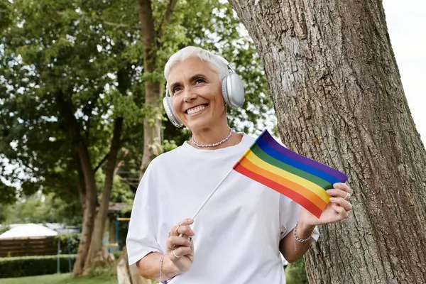 stock image A confident woman celebrates pride with a rainbow flag in a vibrant park.