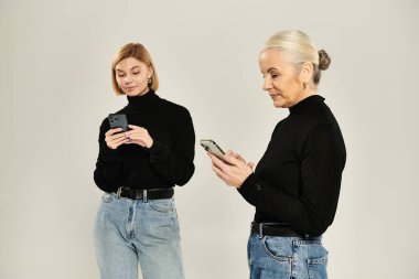 Yetişkin bir kadın ve kızı akıllı telefonlarına birlikte odaklanmışlar..