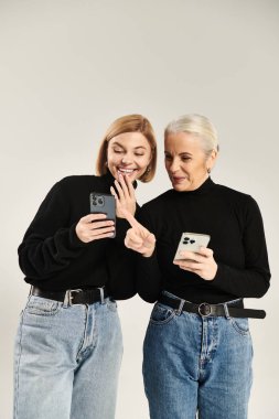 Bir anne ve kızı telefonlarını birlikte kullanırken neşeli bir anı paylaşıyorlar..