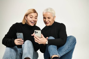 Anne ve kızı telefonlarının keyfini çıkarırken aynı anda gülüyorlar..