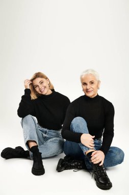 Olgun anne ve kızı, şık kıyafetler içinde birlikte oturarak neşeli bir anı paylaşıyorlar..