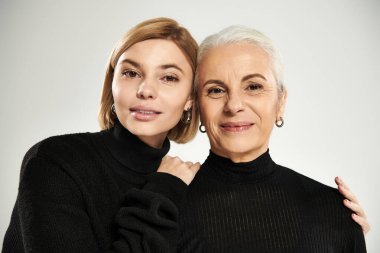 Olgun bir kadın ve yetişkin kızı sıcak bir kucaklaşmayı paylaşıyor..