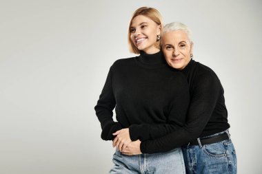 Bir anne kızını kucaklıyor, hem sıcacık gülümsüyor hem de aynı şekilde giyiniyor..