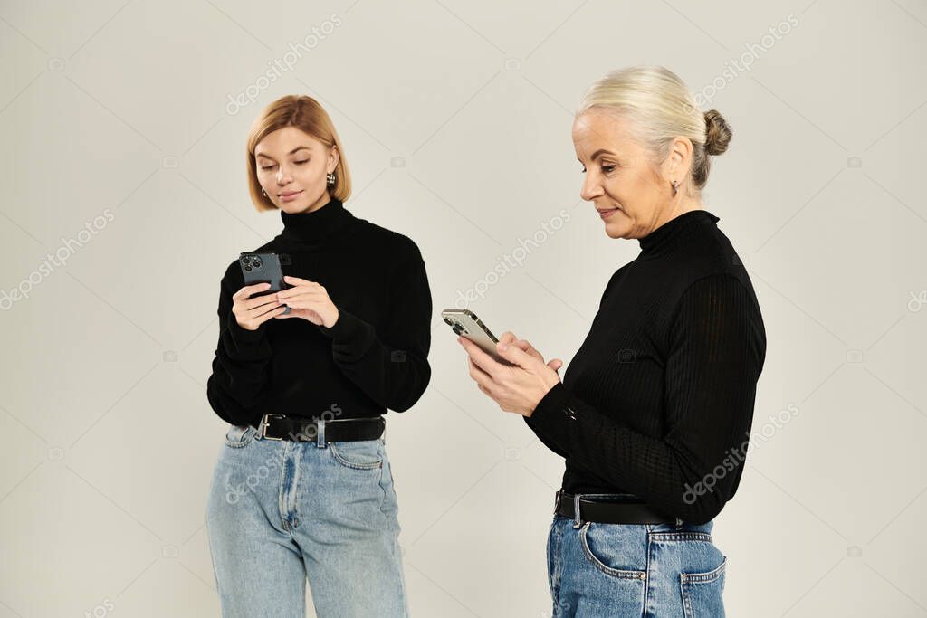 A mature woman and her adult daughter focused on their smartphones together.