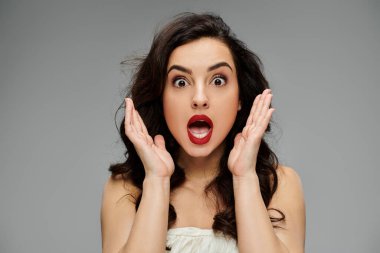 Surprised woman poses gracefully on gray backdrop. clipart