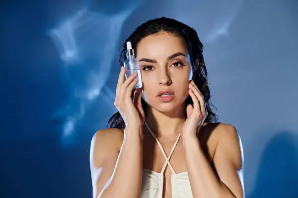 stock image A young woman applies skincare while posing confidently with a bright backdrop.