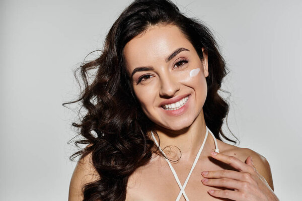A joyful woman applies cream while posing against a colorful background.