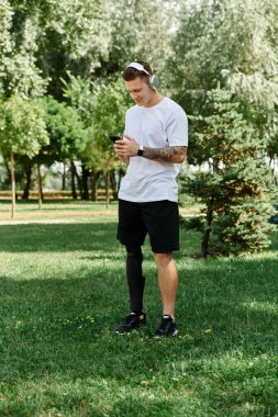 Yapay bacaklı, müzik dinleyen ve güneşli bir parkta telefon kullanan dövmeli bir adam.