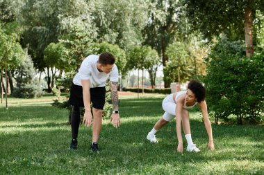 Genç bir kadın ve dövmeli bir adam, canlı bir park ortamında spor ve arkadaşlığı kutluyorlar..