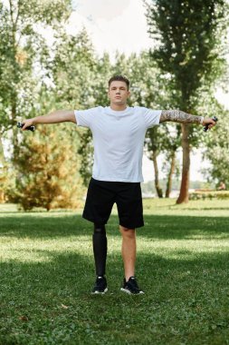 Protez bacaklı dövmeli bir adam yemyeşil bir parkta spor yapıyor..