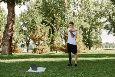 Dövmeli genç adam parkta çalışıyor, online fitness dersi alıyor.