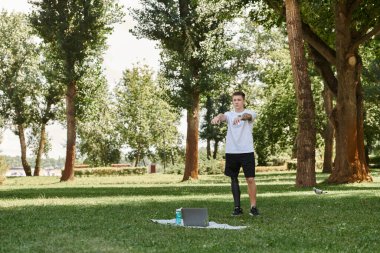 Yeşil Park 'ta çalışan, yapay bacaklı dövmeli genç bir adam online fitness dersi alıyor.