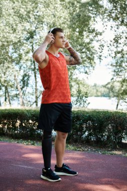 Aktif giyinen dövmeli genç bir adam spor yaparken açık havada şarkı söylüyor.