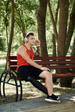 Dövmeli genç bir adam dışarıda bankta oturuyor, kulaklıkla müzik dinlemenin tadını çıkarıyor..