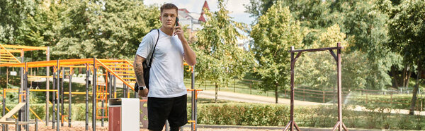 Молодой человек с татуировками гуляет по парку, разговаривает по телефону.