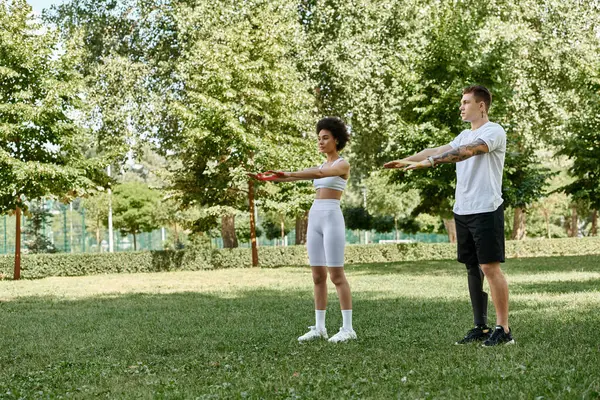 stock image A young woman and a tattooed man engage in a fitness routine surrounded by lush greenery.