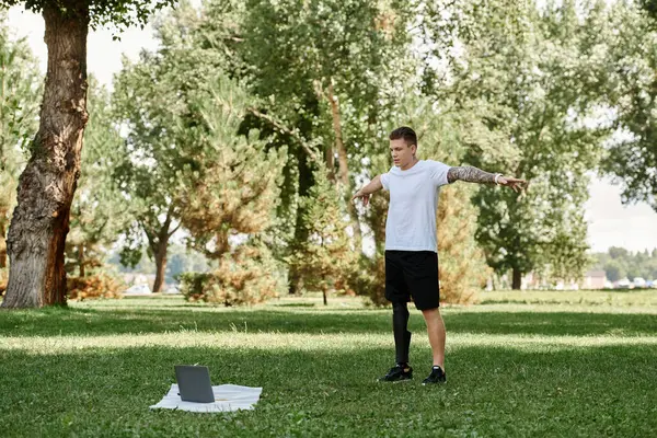 stock image Tattooed young man working out in a park, engaging in an online fitness lesson with determination.