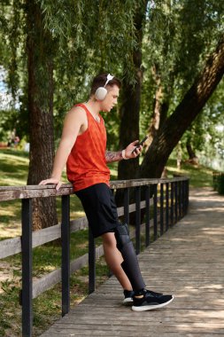 Akıllı telefon kullanan protez bacaklı genç bir adam. Parktaki yeşilliğin etrafını sarmış.