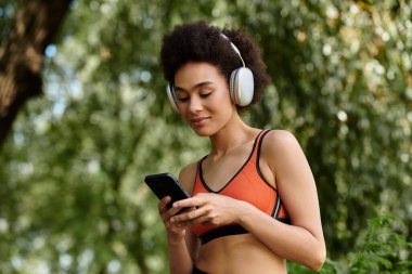 Akıllı telefonda sohbet eden ve parkta kablosuz kulaklıkla müzik dinleyen genç bir kadın.