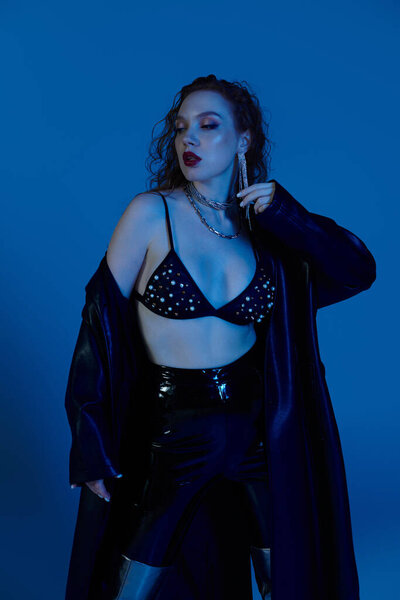 A confident woman displays her stylish ensemble against a captivating blue setting.