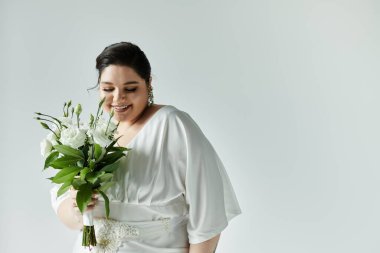 Işıl ışıl ve iri bir gelin buketini zevkle tutar, güzel beyaz elbisesini ve küpelerini gösterir..