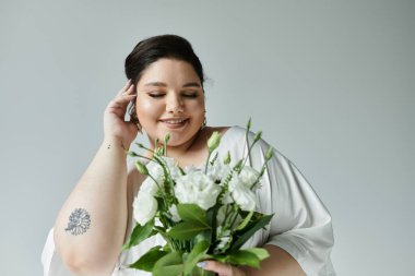 A beautiful bride in a white dress smiles softly, holding a bouquet of white roses on a neutral grey background. clipart