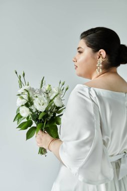 A stunning plus size bride showcases her elegant wedding attire and bouquet against a soft grey backdrop. clipart