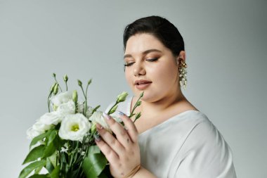 A stunning plus size bride admires her bouquet, radiating grace in a flowing white gown with delicate earrings. clipart