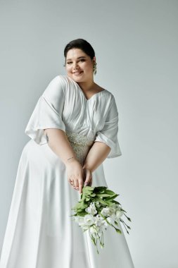 Neşeli ve iri bir gelin zarif bir şekilde güzel beyaz elbisesini gösterirken elinde güzel bir buket.
