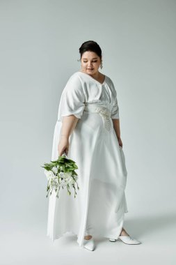 Büyüleyici, iri yarı bir gelin zarif bir şekilde buketini tutar. Beyaz elbisesinin içinde zarafetini sergiler..