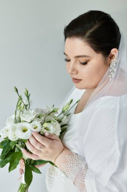 Güzel, iri yarı bir gelin, narin gelinliğiyle süslenmiş beyaz bir buketi nazikçe besler..