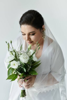 A beautiful young bride in a flowing white gown holds a bouquet, radiating joy and elegance. clipart