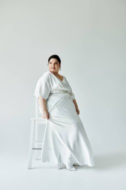 Güzel, iri cüsseli bir gelin, parlak küpelerle süslenmiş beyaz elbisesiyle zarafet saçar..